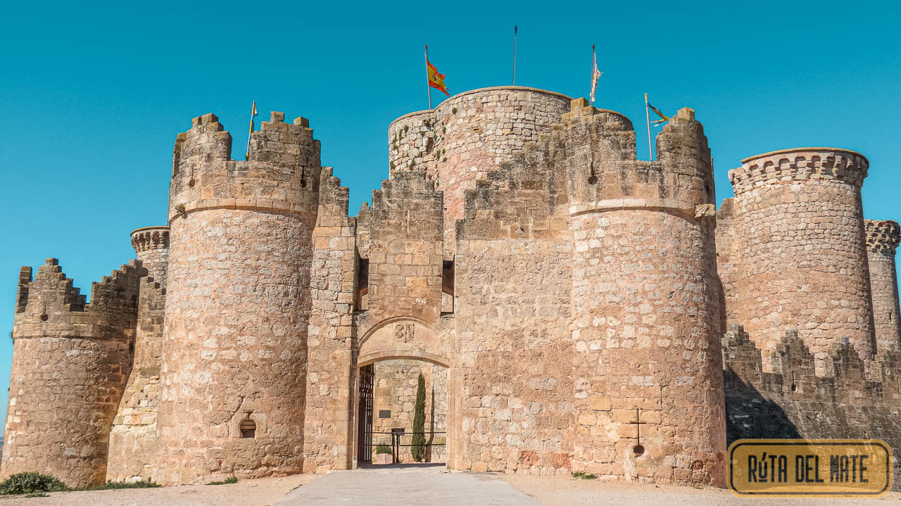 Puerta de acceso para visitar el Castillo de Belmonte: vista desde afuera, con sus torres de vigilancia. La fachada se encuentra iluminada por el sol, el cielo está bien celeste.
