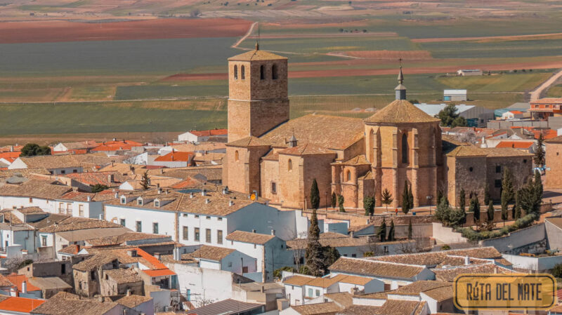 Vista aérea, desde el castillo, de la Colegiata San Bartolomé. La colegiata se alza y destaca por sobre las casas bajas del pueblo de Belmonte y, más allá, se observa La Mancha. 