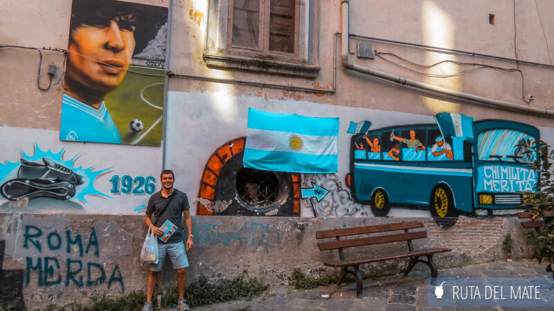 Juan junto a grafitis, un mural de Maradona y la bandera argentina en las calles de Napoles