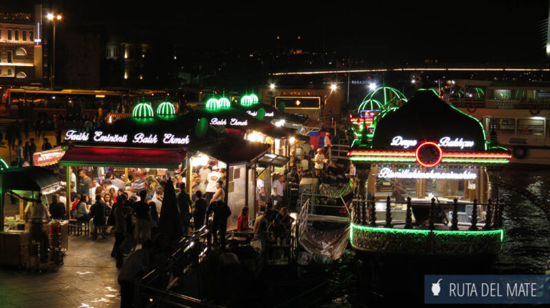 La orilla del puente Galata de noche, con bares y puestos de comida iluminados