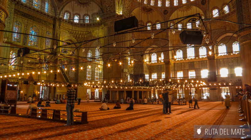 El interior de la Mezquita Azul, donde se ve gente rezando sobre una alfombra roja.