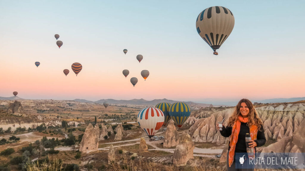 Flor, mate en mano, en Capadocia, detrás los globos aerostáticos saliendo. Descubre todos los consejos para visitar este país en la guía para viajar a Turquía.