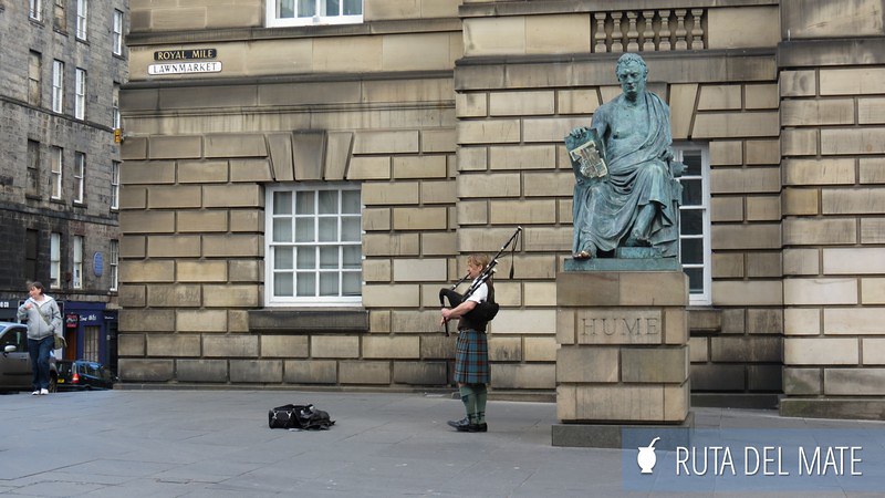 Estatua del filósofo escocés David Hume junto a una persona tocando la gaita en Edimburgo