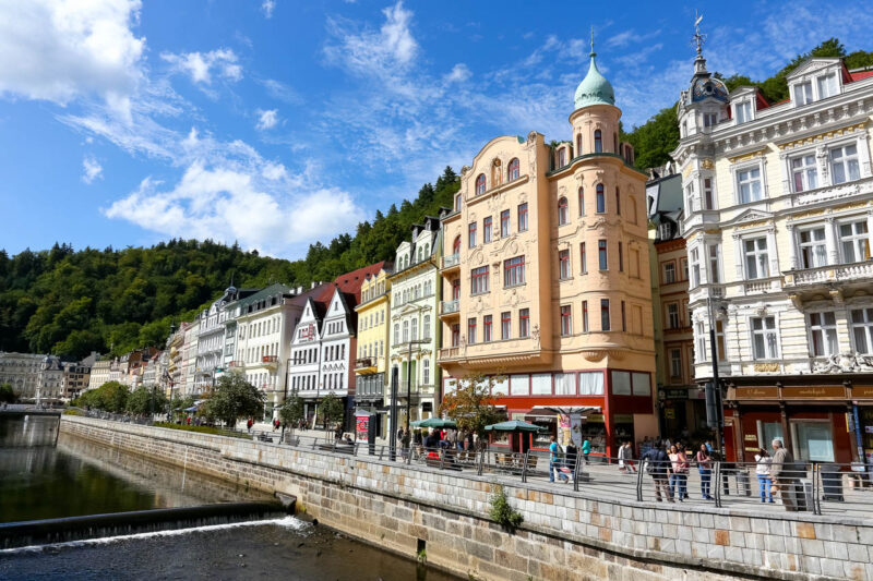 Esta ciudad cerca de Praga es Karlovy Vary, y se ven las fachadas típicas de las casas en la rivera del río, con gente caminando, paseando y de compras.