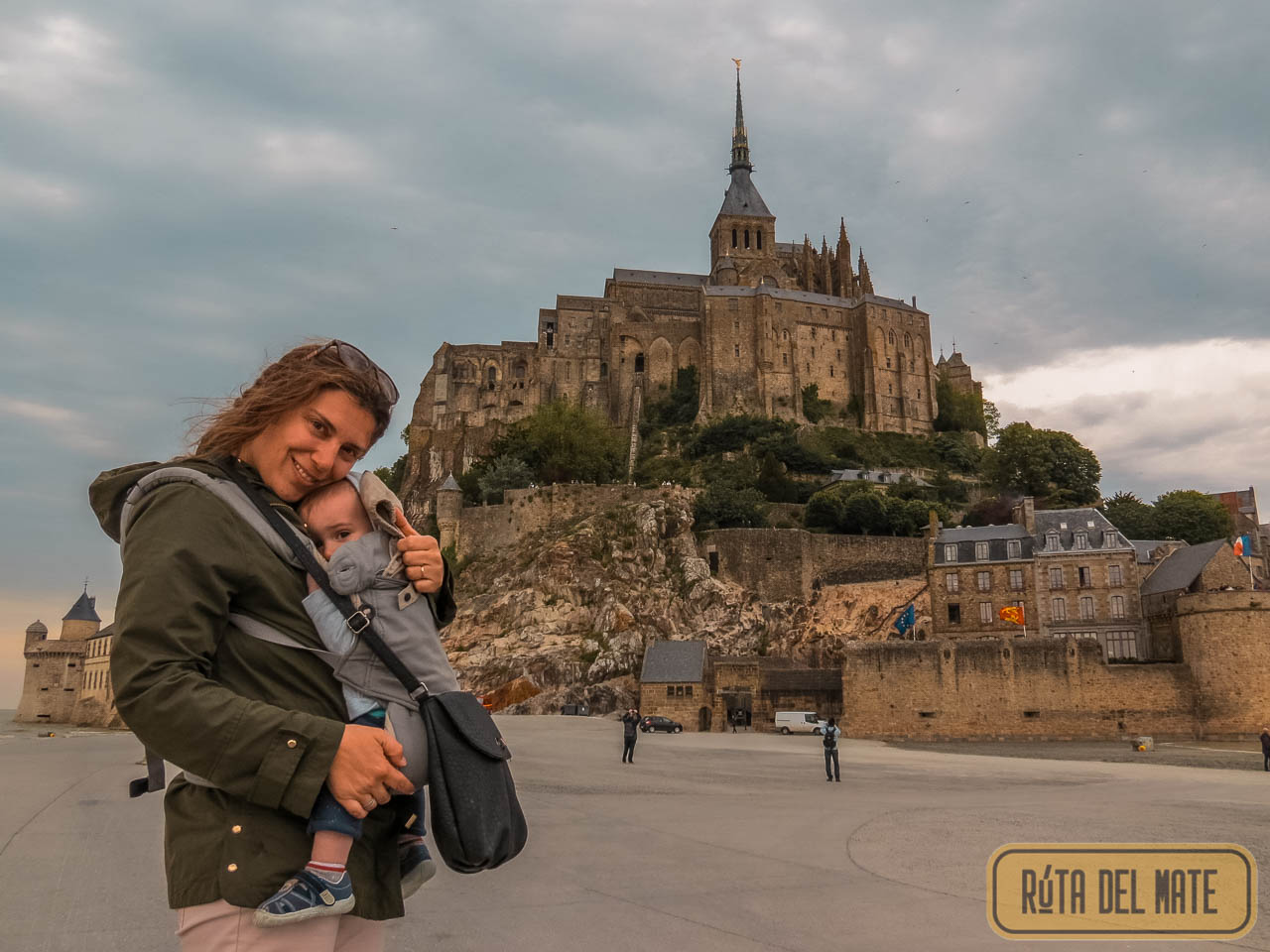 Flor carrying Benja in a baby carrier in front of Mont Saint-Michel